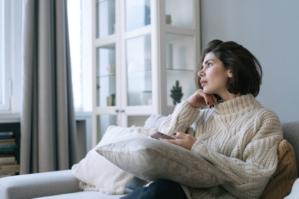 Woman sitting quietly with a phone nearby showing the benefits of boredom for reflection and mental space.