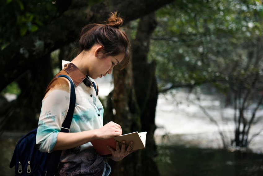 Woman writing in a notebook outdoors to show where good ideas come from through quiet reflection.